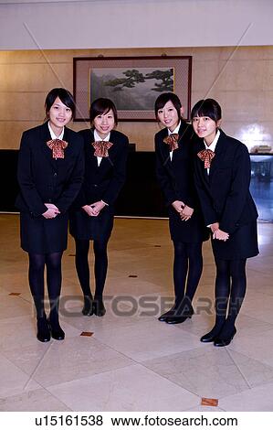 Stock Photo - Four waitress gesturing with hands folded in front and smiling at the camera. Fotosearch