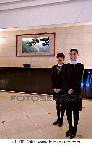 Stock Image - Two young waitress standing with hands folded in front and smiling at the camera. Fotosearch
