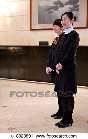 Stock Image - Two young waitress standing with hands folded in front and looking away. Fotosearch