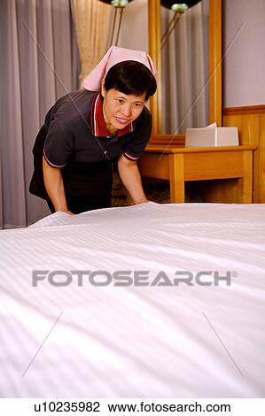 Stock Image - Waitress tidying the bed in the room. Fotosearch