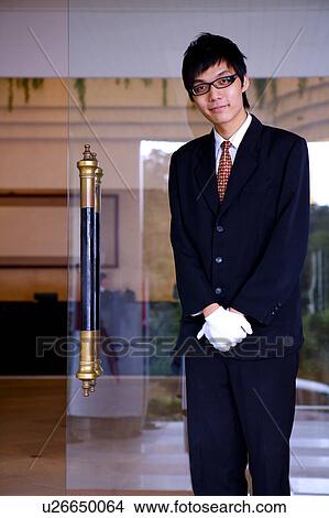 Young waiter standing with hands folded in front and looking at the camera View Large Photo Image Picture - Young waiter standing with hands folded in front and looking at the camera. Fotosearch