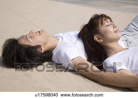 Stock Image - Japanese couple lying on a beach. Fotosearch