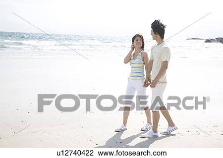 Stock Image - Japanese couple walking on a beach. Fotosearch