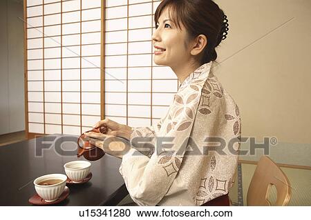 Stock Image - Japanese woman putting on kimono. Fotosearch