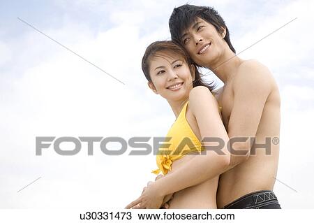Stock Image - Japanese man embraces lover from back. Fotosearch