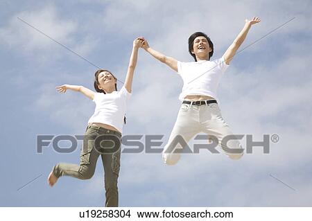 Picture - Jumping Japanese couple below the blue sky. Fotosearch