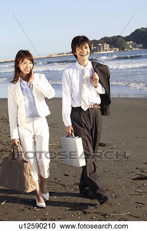 Stock Image - Japanese couple walking along a beach. Fotosearch
