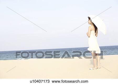 Stock Image - Japanese woman put up an sunshade on the beach. Fotosearch