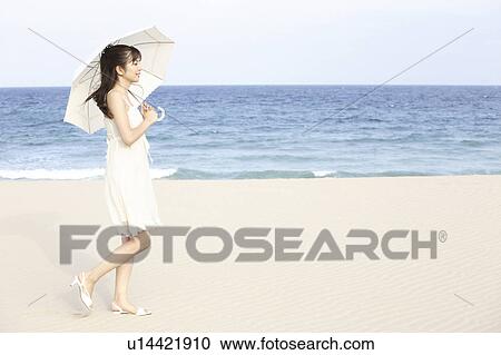Stock Image - Japanese woman put up an sunshade on the beach. Fotosearch