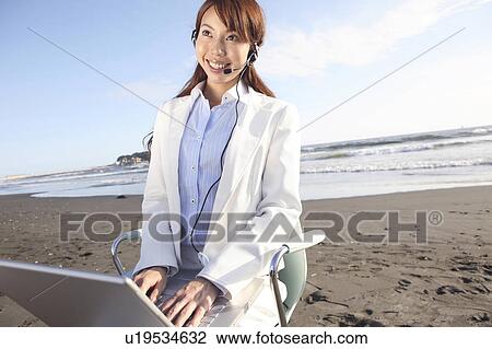 Stock Image - Office lady operating a PC on a beach. Fotosearch
