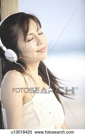 Stock Photography - Japanese woman listening to music on a beach. Fotosearch