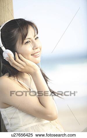 Stock Photography - Japanese woman listening to music on a beach. Fotosearch