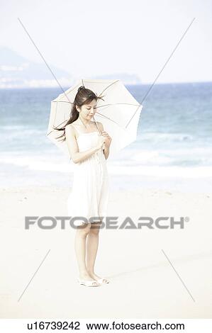 Stock Image - Japanese woman put up an sunshade on the beach. Fotosearch