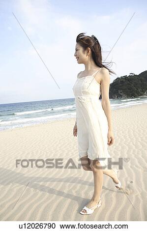 Stock Image - Japanese woman walking along a beach. Fotosearch