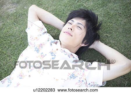 Stock Image - Japanese man lying down on the grass. Fotosearch