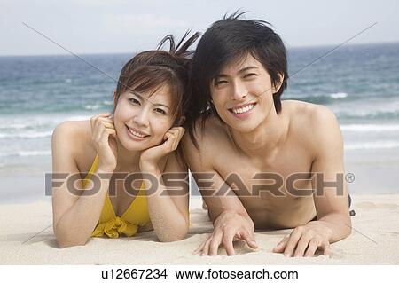 Japanese couple lying on a beach in swimsuit View Large Photo Image Picture - Japanese couple lying on a beach in swimsuit. Fotosearch