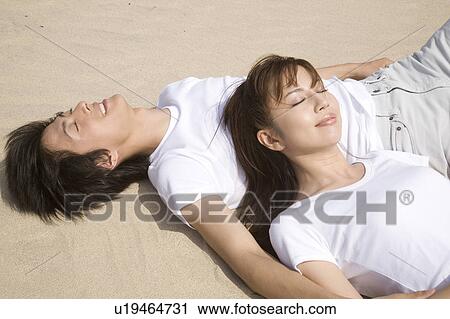 Stock Image - Japanese couple lying on a beach. Fotosearch
