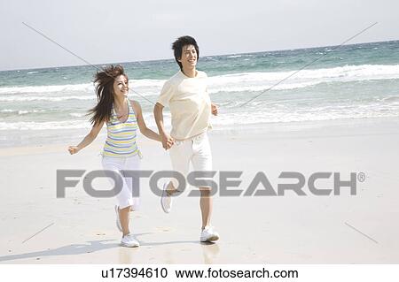 Stock Image - Japanese couple running on a beach. Fotosearch