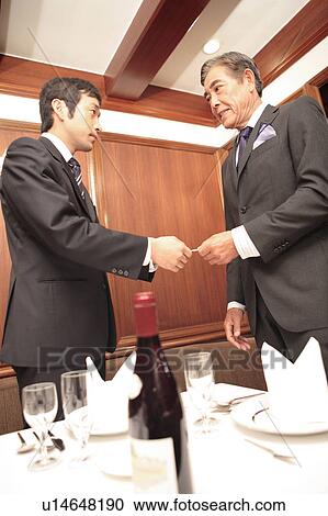 Stock Image - Japanese office workers exchanging business cards. Fotosearch