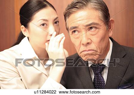 Stock Image - Office lady talking secretively to executive. Fotosearch