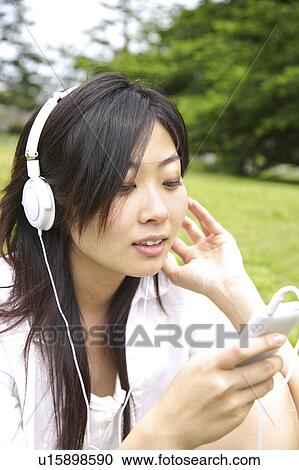 Stock Image - Japanese woman listening to music in a park. Fotosearch