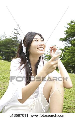 Stock Image - Japanese woman listening to the music in a park. Fotosearch