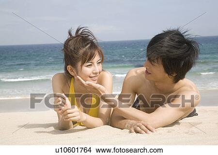 Picture - Japanese couple lying on a beach in swimsuit. Fotosearch