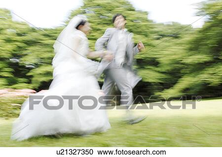 Stock Image - Bridal couple running in garden. Fotosearch