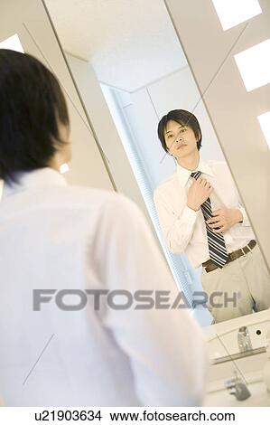 Picture - Business man putting on a necktie in rest room. Fotosearch