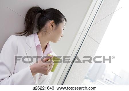 Stock Image - Business woman looking at outside and having a cup of coffee. Fotosearch