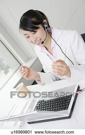 Stock Image - Business woman putting on a headset. Fotosearch
