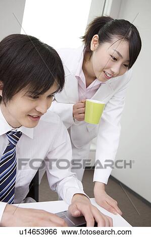 Office worker operating a PC and coworker looking at monitor from behind View Large Photo Image Stock Photograph - Office worker operating a PC and coworker looking at monitor from behind. Fotosearch