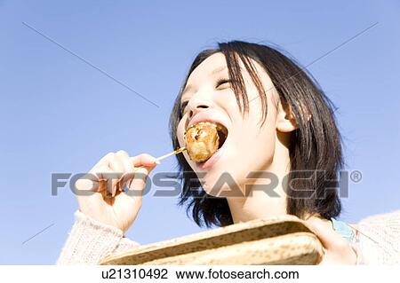Stock Image - Woman eating Takoyaki. Fotosearch