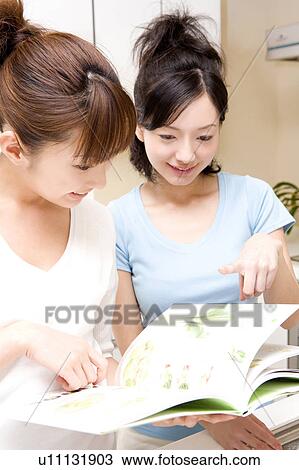 Stock Image - Japanese women reading a cooking book. Fotosearch