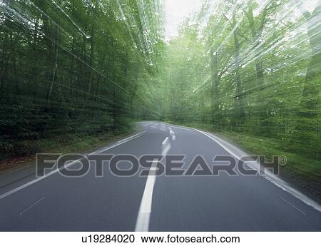 Stock Image - Blurred road through forest. Fotosearch