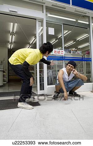 Stock Image - Convenience store clerk talking to young man. Fotosearch