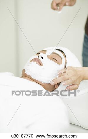 Stock Image - Young man receiving facial pack. Fotosearch