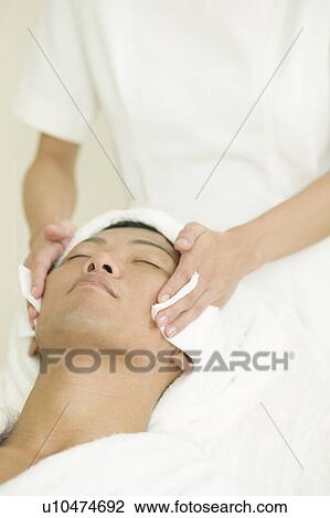 Stock Image - Young man receiving facial treatment. Fotosearch