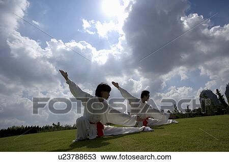 Stock Image - Young man and woman doing kung-fu moves against cloudy sky. Fotosearch