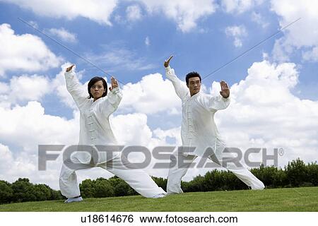Stock Photograph - Young man and woman doing kung-fu moves against sky. Fotosearch