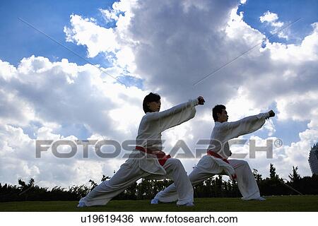Stock Photograph - Young man and woman doing kung-fu moves against cloudy sky. Fotosearch