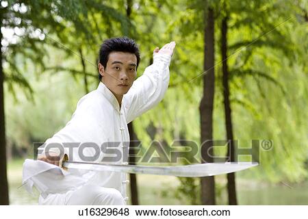 Stock Photo - Young man in martial arts pose in park. Fotosearch