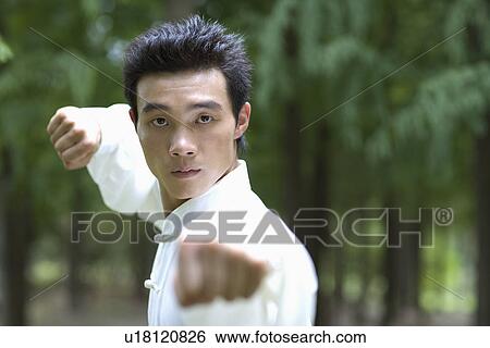 Stock Photograph - Young man wearing martial arts uniform performing the Kung Fu punching. Fotosearch