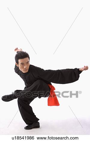 Stock Photograph - Young man wearing martial arts uniform performing the Kung Fu eagle stance. Fotosearch