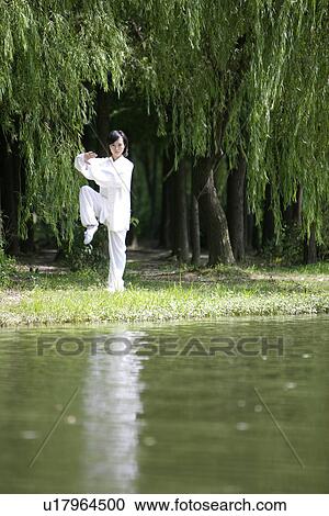 Stock Image - Young woman doing kung-fu moves at water's edge. Fotosearch