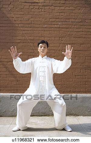 Stock Image - Man doing Tai Chi in front of surrounding wall. Fotosearch