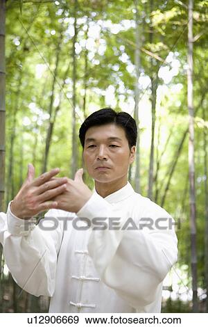 Stock Photo - Man practicing Tai Chi amongst trees, portrait. Fotosearch