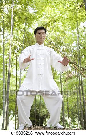 Stock Photo - Man practicing Tai Chi amongst trees, portrait. Fotosearch