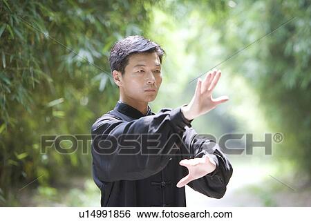 Stock Photograph - Mature man practicing Tai Chi in bamboo grove. Fotosearch