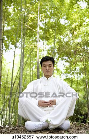 Stock Photo - Mature man sitting with legs crossed on bamboo grove. Fotosearch